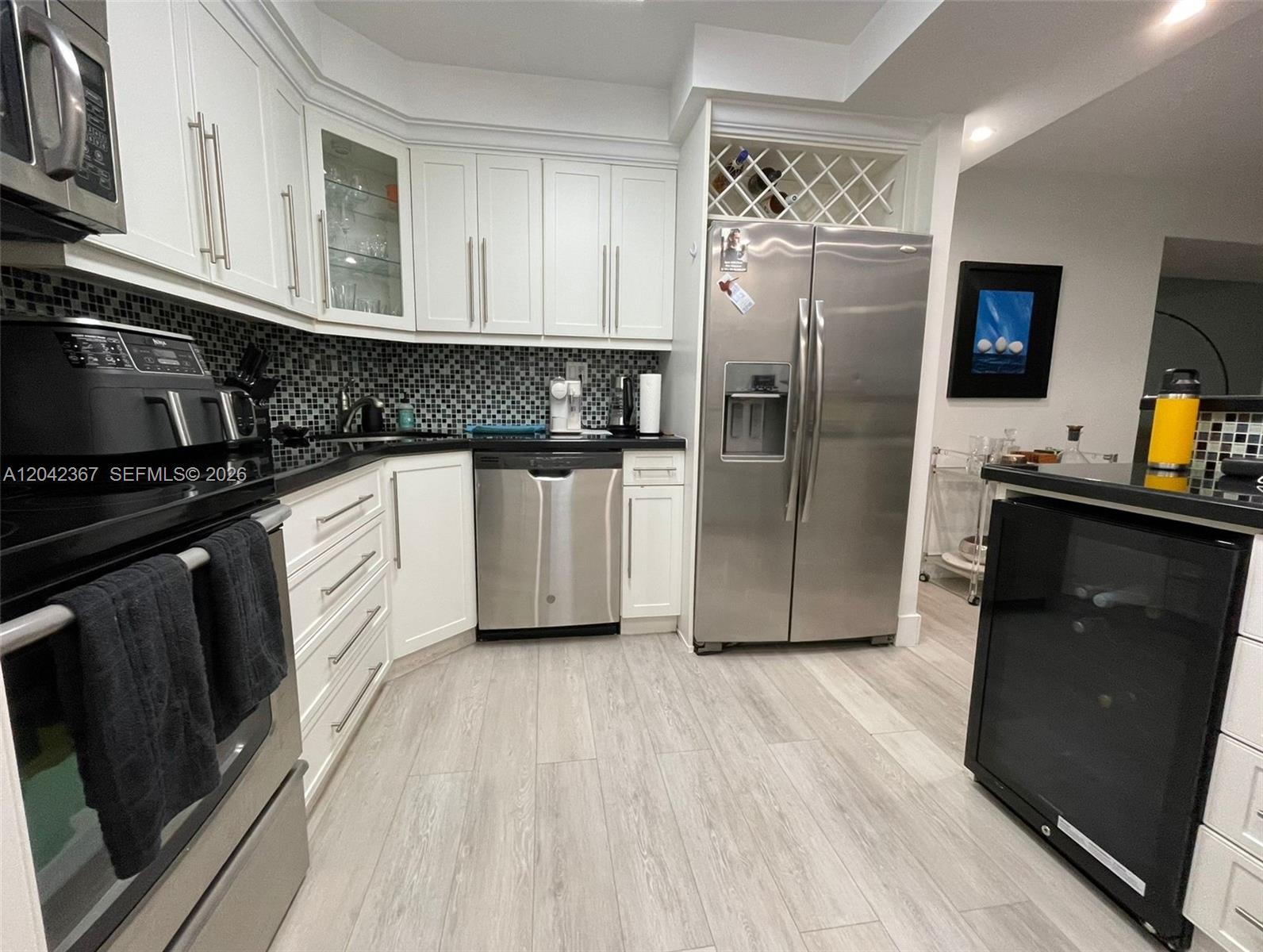 A kitchen features white cabinets, stainless steel appliances, black countertops, and a mosaic tile backsplash — 2333 Brickell Ave # 314, Miami FL 33129, MIAMI, FL