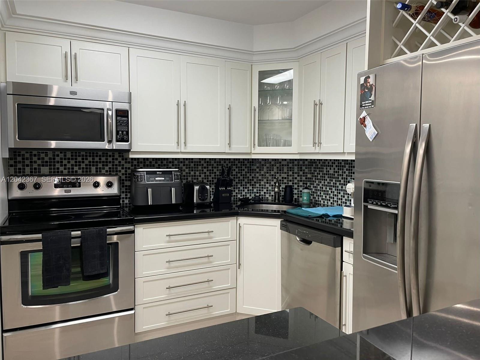 A kitchen features white cabinets, stainless steel appliances, and a black tiled backsplash — 2333 Brickell Ave # 314, Miami FL 33129, MIAMI, FL