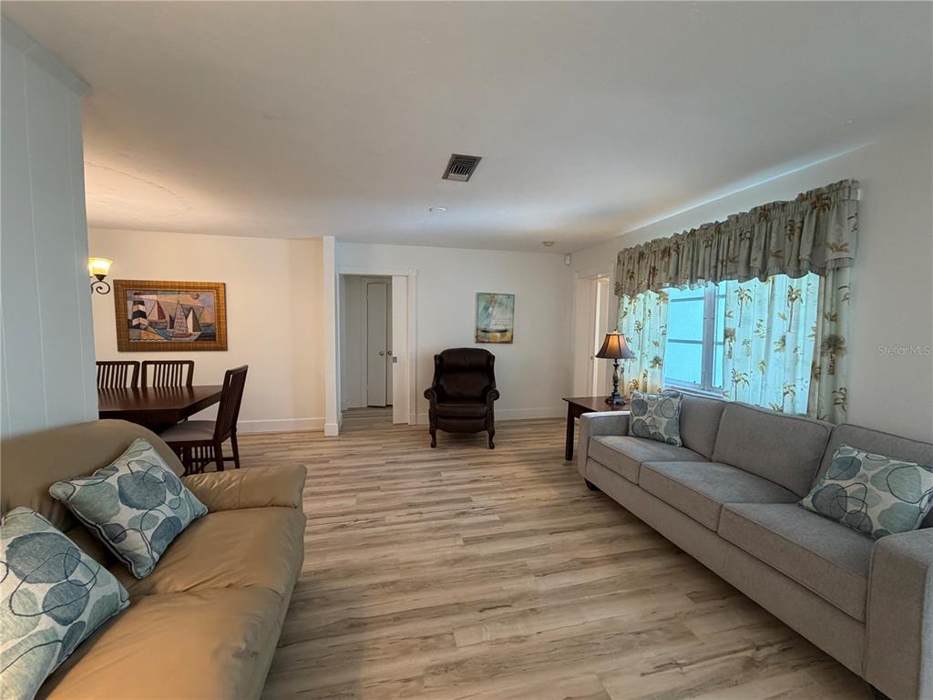 A living room with light wood-look flooring, a gray sofa, and a dining area — 732 SANTA MARGERITA LANE, PUNTA GORDA, FL