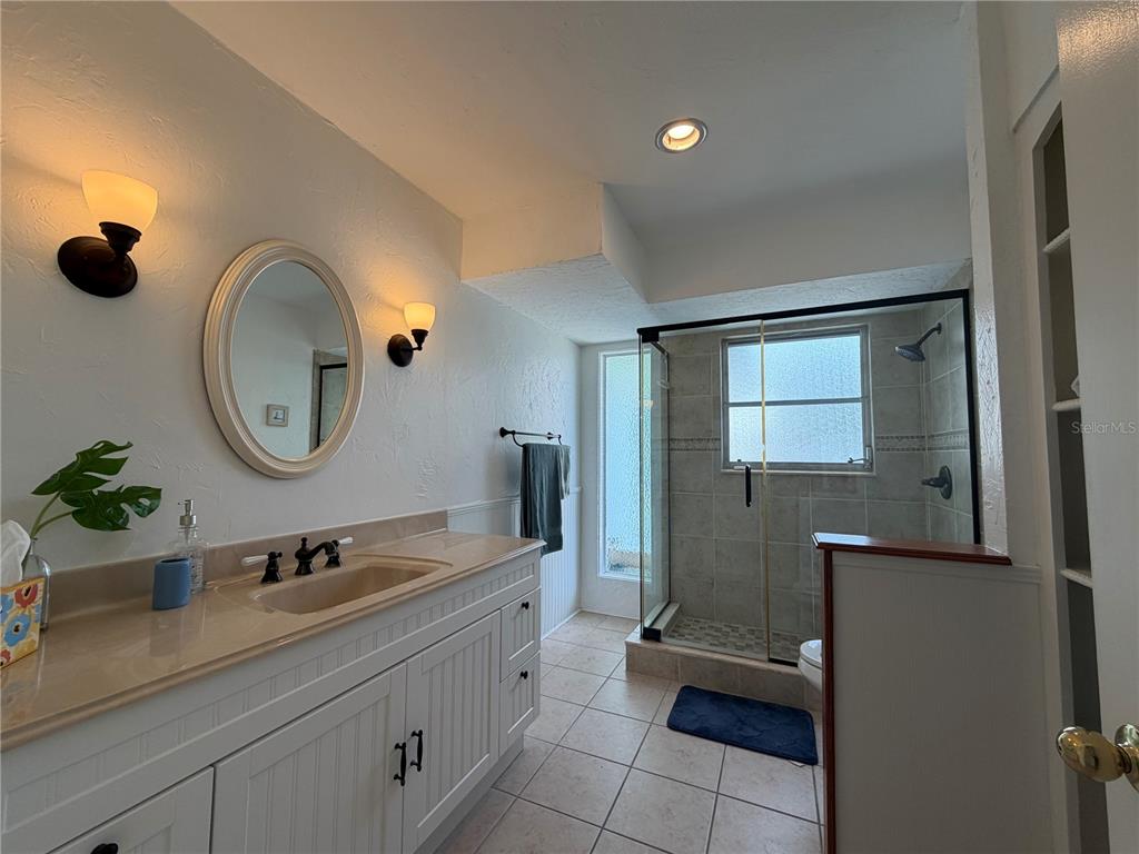 A bathroom features a white vanity, an oval mirror, and a tiled walk-in shower — 732 SANTA MARGERITA LANE, PUNTA GORDA, FL