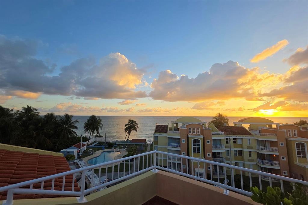 A balcony view overlooking a swimming pool, palm trees, and the ocean at sunset — CII EL CHARLIE UNIT G405, LOIZA, PR