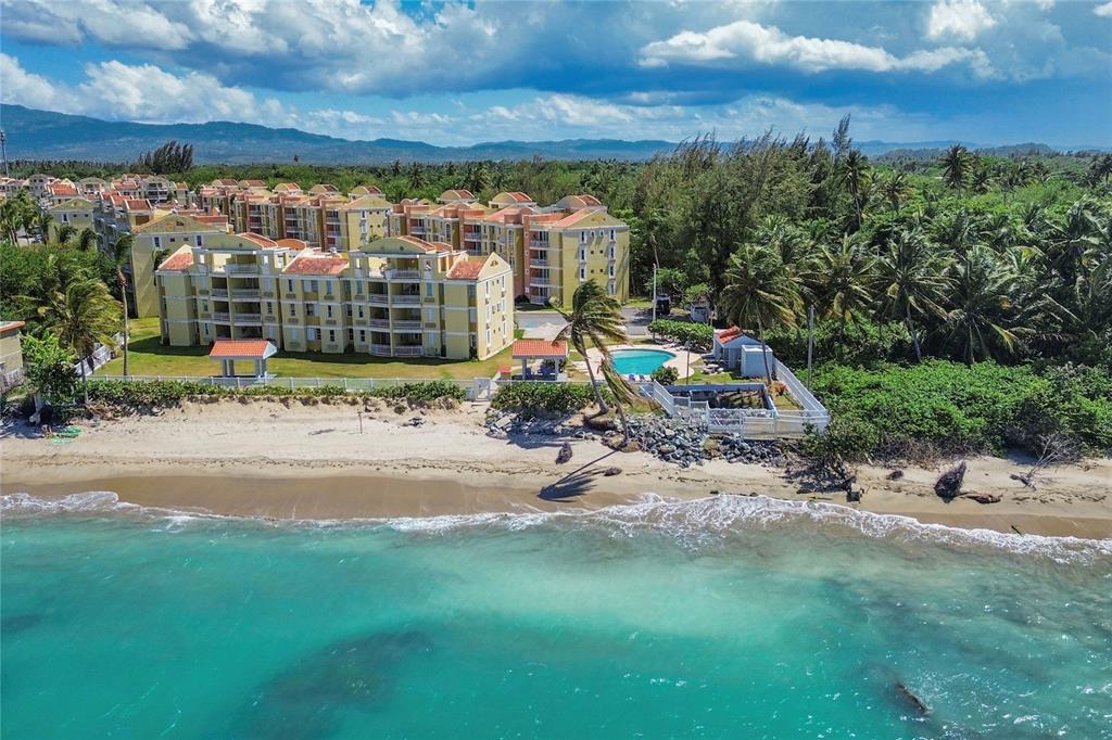 An aerial view shows a yellow apartment complex located directly on a sandy beach — CII EL CHARLIE UNIT G405, LOIZA, PR