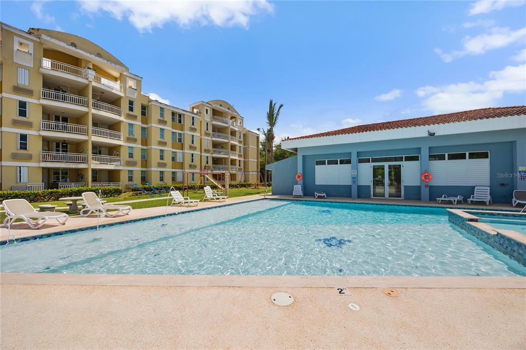 A swimming pool sits in front of a multi-story apartment building and a clubhouse — CII EL CHARLIE UNIT G405, LOIZA, PR