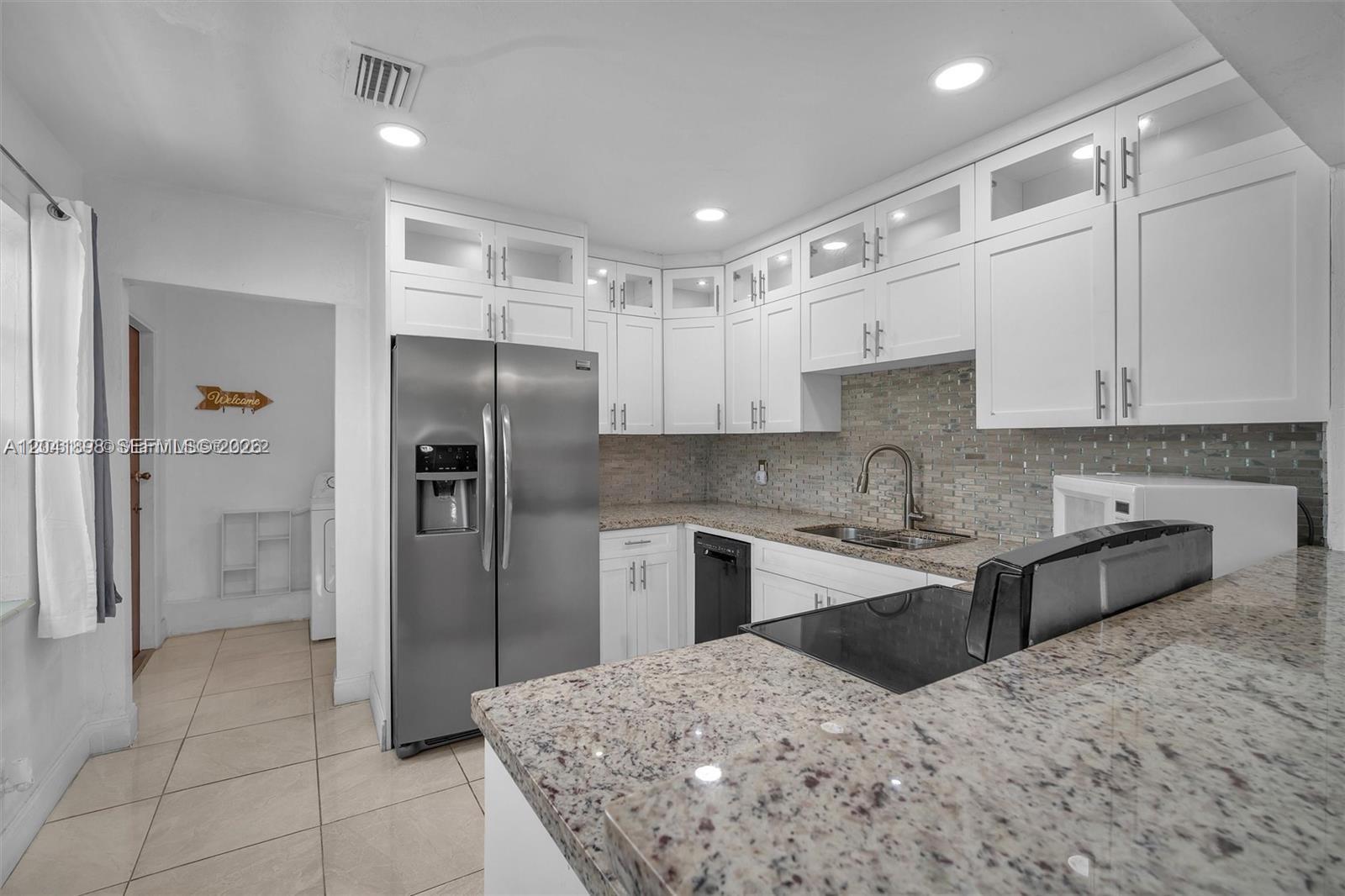 A kitchen features white cabinetry, granite countertops, stainless steel appliances, and a tiled backsplash — 1635 Hollywood Blvd, Hollywood FL 33020, HOLLYWOOD, FL