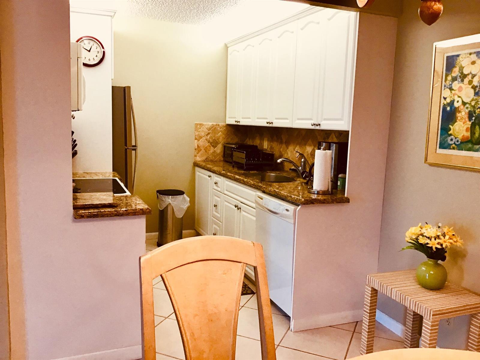 A small kitchen features white cabinets, granite countertops, a tiled backsplash, and a white dishwasher — 4008 Cornwall A, Boca Raton FL 33434, BOCA RATON, FL
