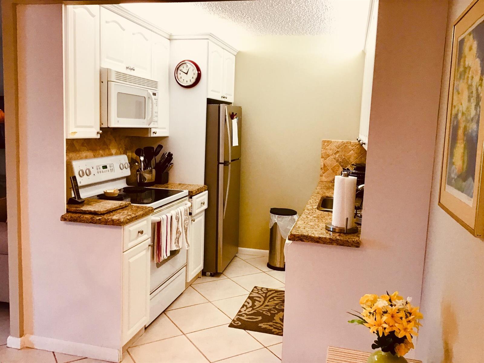 A kitchen features white cabinetry, granite countertops, stainless steel appliances, and tile flooring — 4008 Cornwall A, Boca Raton FL 33434, BOCA RATON, FL