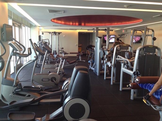 This gym features rows of exercise equipment, a circular red ceiling light, and floor-to-ceiling windows — 55 SE 6th St # 2106, Miami FL 33131, MIAMI, FL