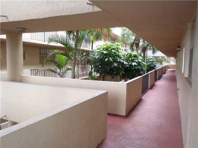 An outdoor walkway with a red floor overlooks a courtyard with palm trees and greenery — 403 NW 68th Avenue # 519, Plantation FL 33317, PLANTATION, FL