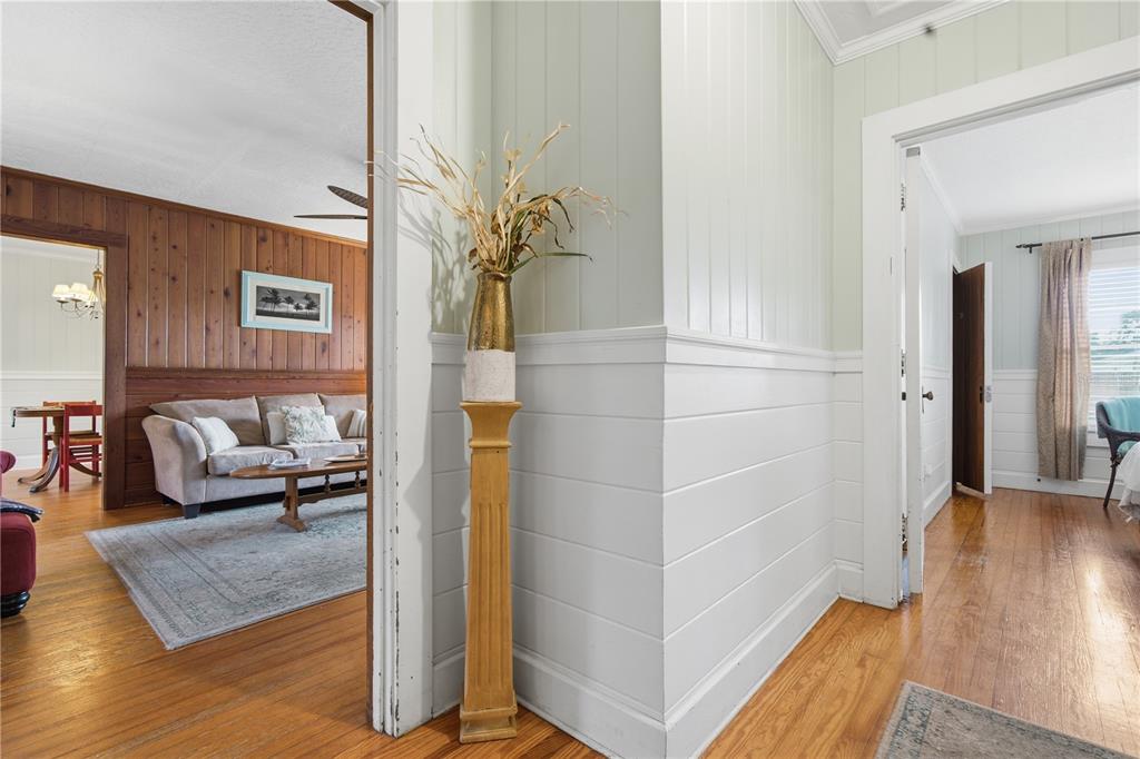 A hallway with white wainscoting leads to a living room with wood-paneled walls — 411 W 48TH STREET, BRADENTON, FL