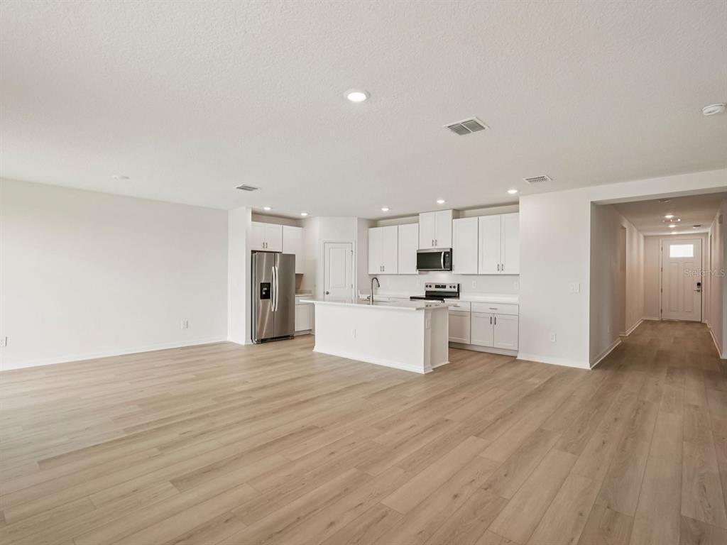 An open-concept kitchen with white cabinets, stainless steel appliances, and light wood-look flooring — 10417 ABUNDANCE GROVE WAY, PARRISH, FL