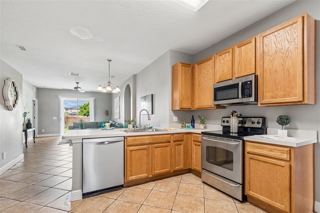 A kitchen with oak cabinets, stainless steel appliances, and tile flooring opens to a living area — 27211 LIRIOPE COURT, WESLEY CHAPEL, FL