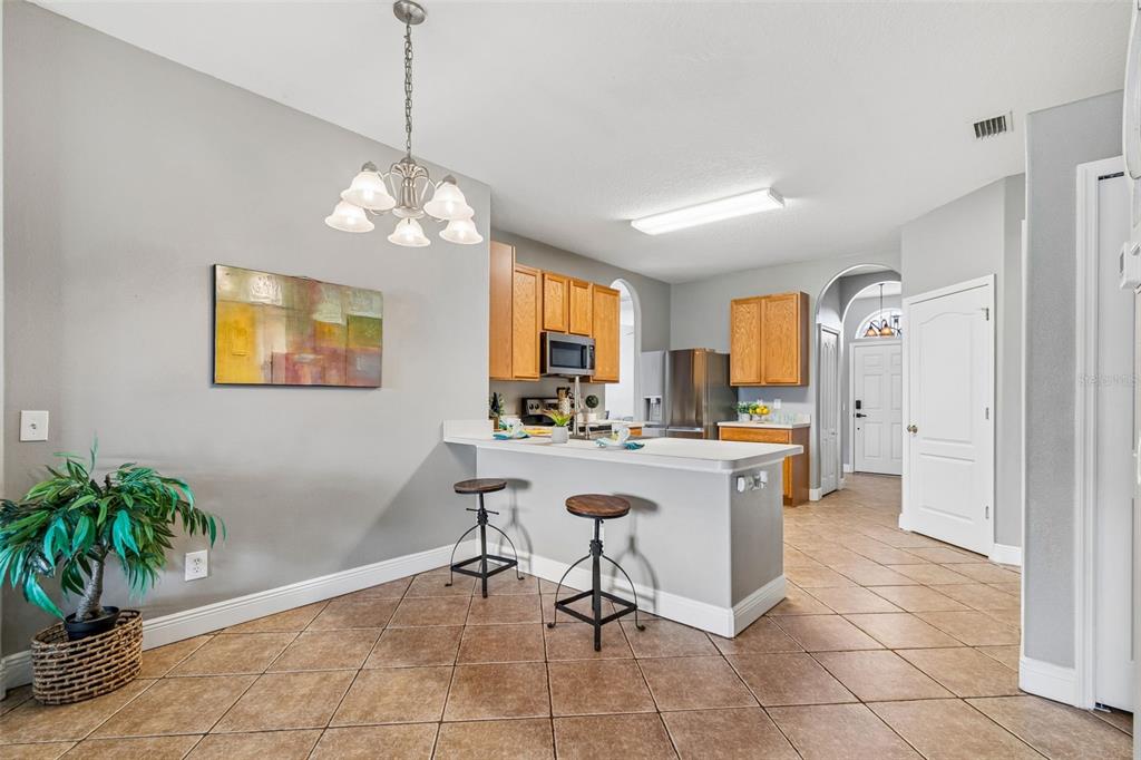 A kitchen with oak cabinets, a breakfast bar with two stools, and tile flooring — 27211 LIRIOPE COURT, WESLEY CHAPEL, FL