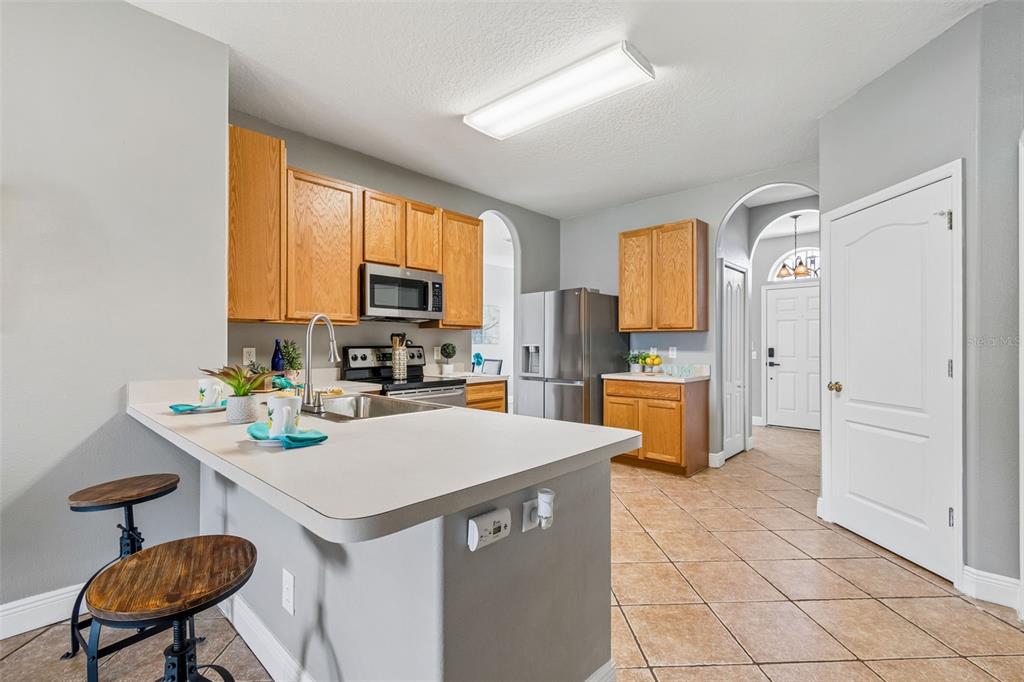 A kitchen features light-colored countertops, wooden cabinets, stainless steel appliances, and tile flooring — 27211 LIRIOPE COURT, WESLEY CHAPEL, FL
