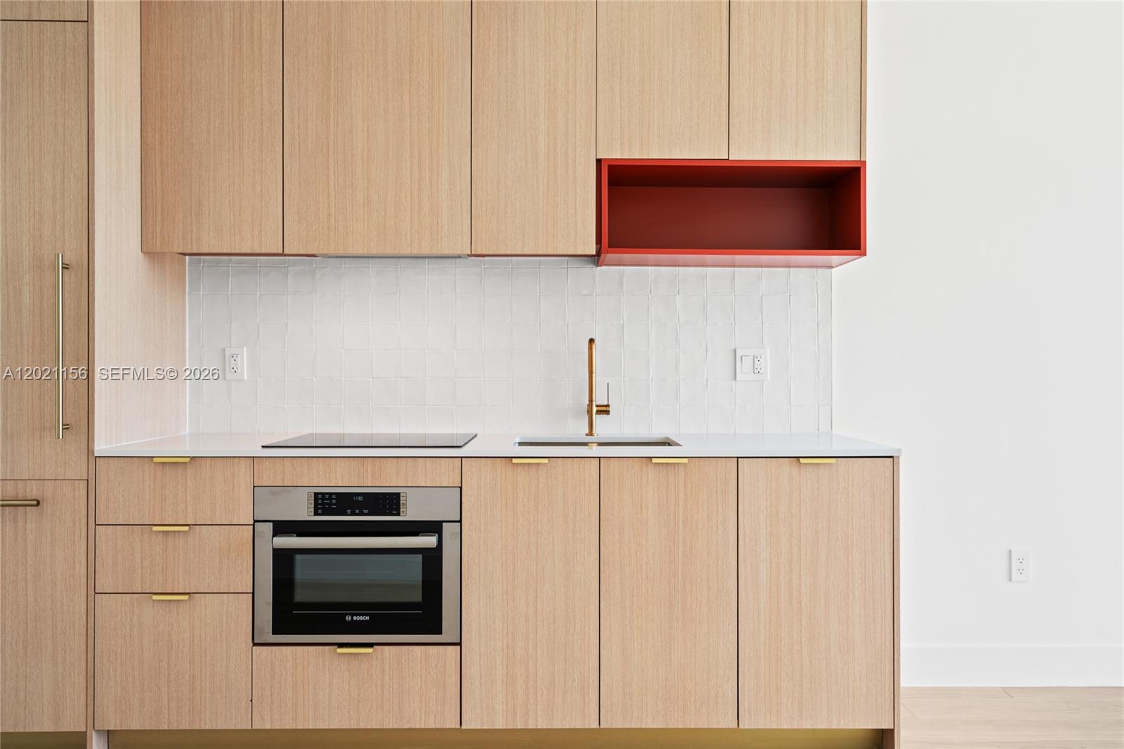 A modern kitchen features light wood cabinets, a red open shelf, and a white backsplash — 90 NE 32nd St # 627, Miami FL 33137, MIAMI, FL