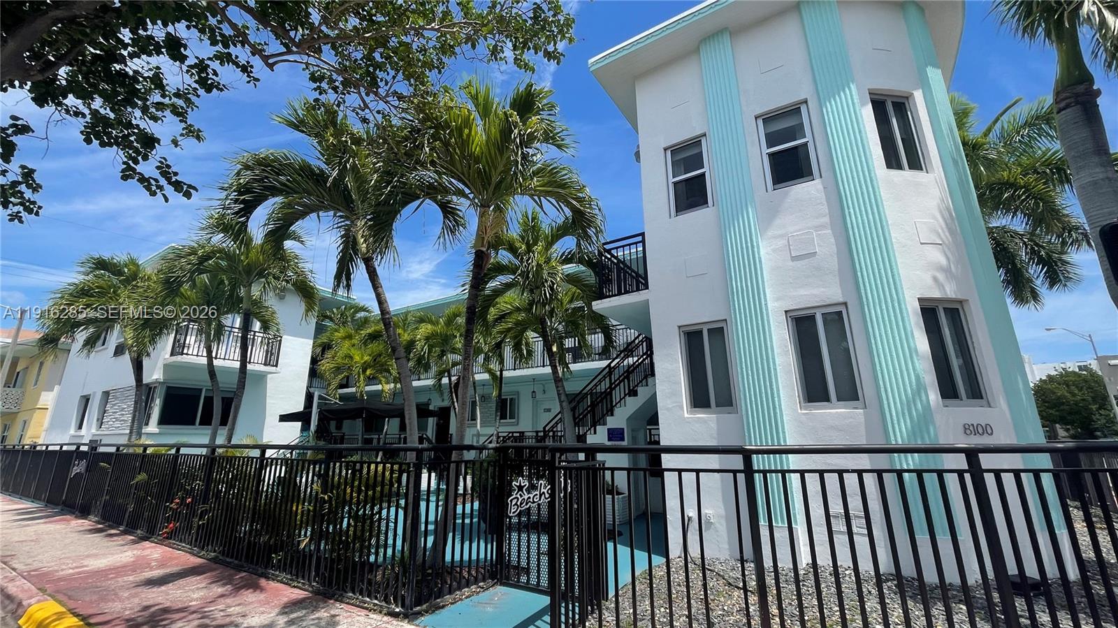 A multi-story white building with teal accents and palm trees stands behind a black fence — 8100 Harding Ave # 508, Miami Beach FL 33141, MIAMI BEACH, FL