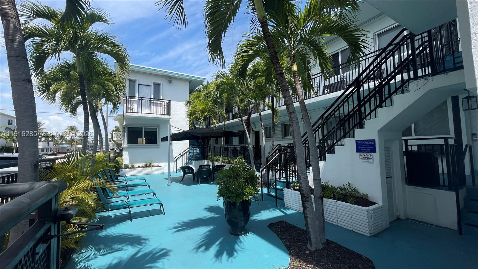 A blue-painted courtyard features palm trees, lounge chairs, a patio table, and exterior staircases — 8100 Harding Ave # 508, Miami Beach FL 33141, MIAMI BEACH, FL