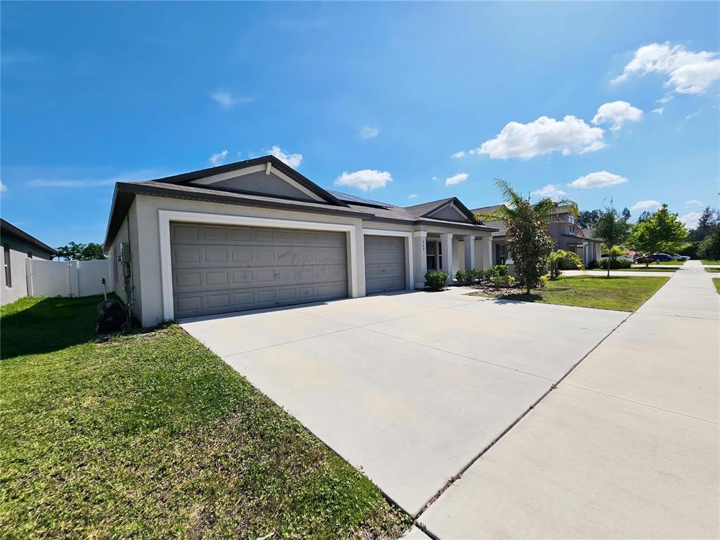 A single-story house features a three-car garage, a concrete driveway, and a covered entryway — 165 RAIN BERRY AVENUE, RUSKIN, FL