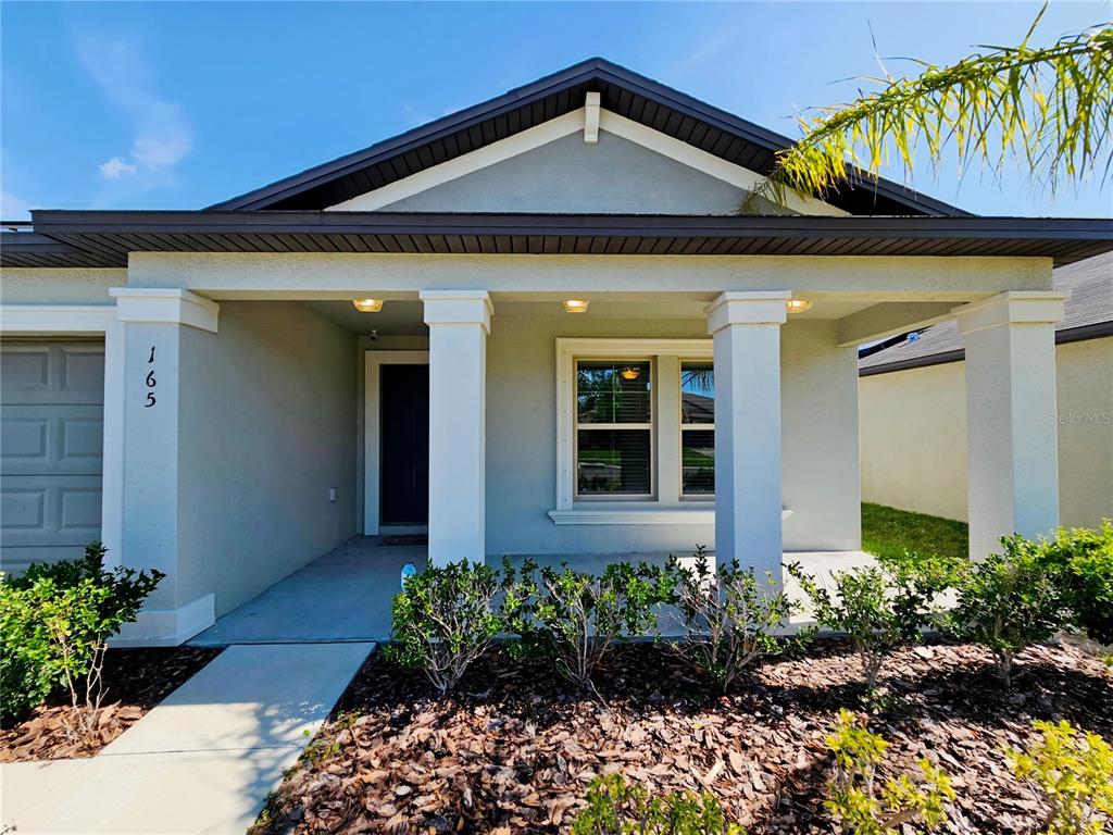 The front exterior of a single-story house features a covered porch with white columns — 165 RAIN BERRY AVENUE, RUSKIN, FL