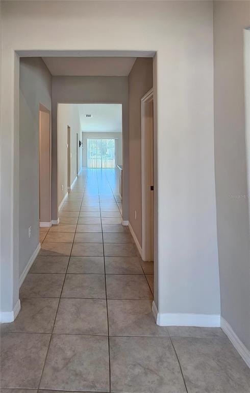 A tiled hallway leads from an entryway toward a distant room with sliding glass doors — 165 RAIN BERRY AVENUE, RUSKIN, FL