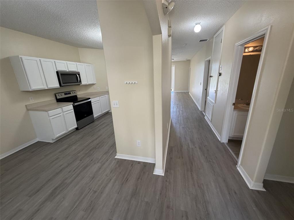 A kitchen with white cabinets and stainless steel appliances opens into a hallway with flooring — 311 SUNSET VIEW DRIVE, DAVENPORT, FL