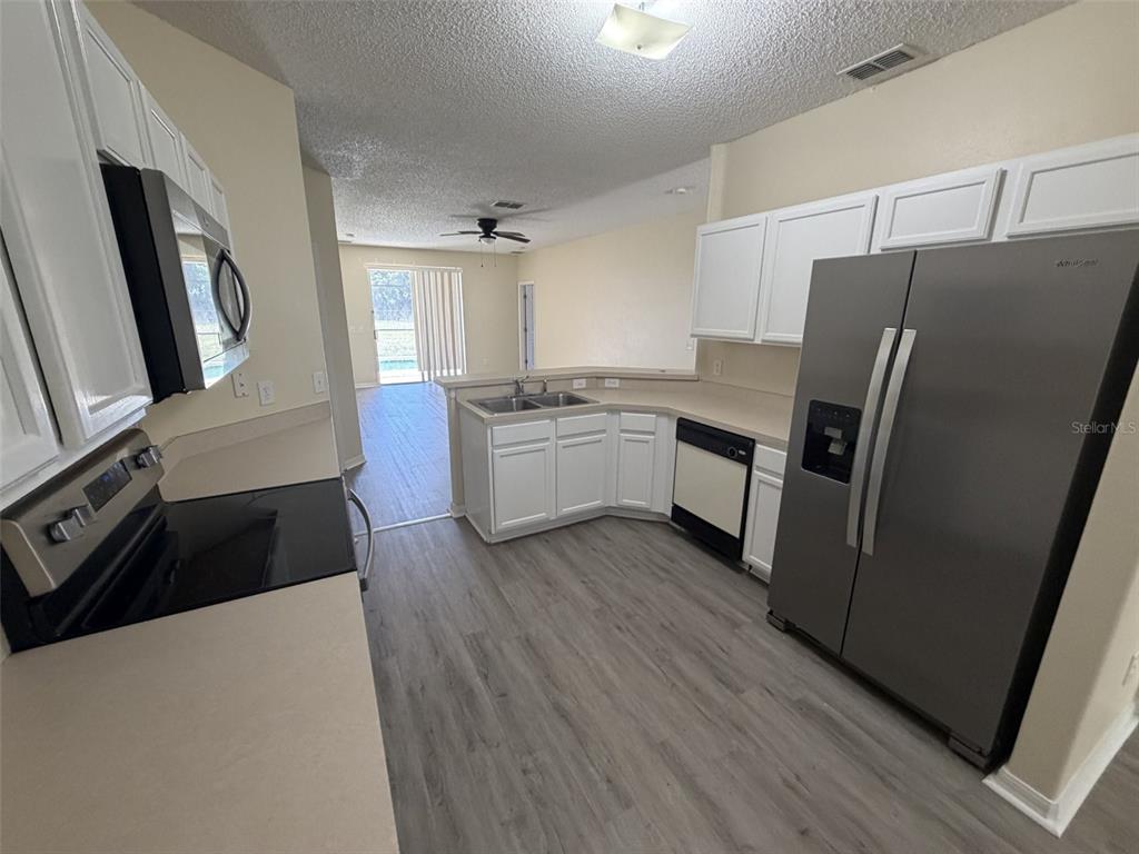 A kitchen features white cabinets, stainless steel appliances, and light wood-look flooring — 311 SUNSET VIEW DRIVE, DAVENPORT, FL