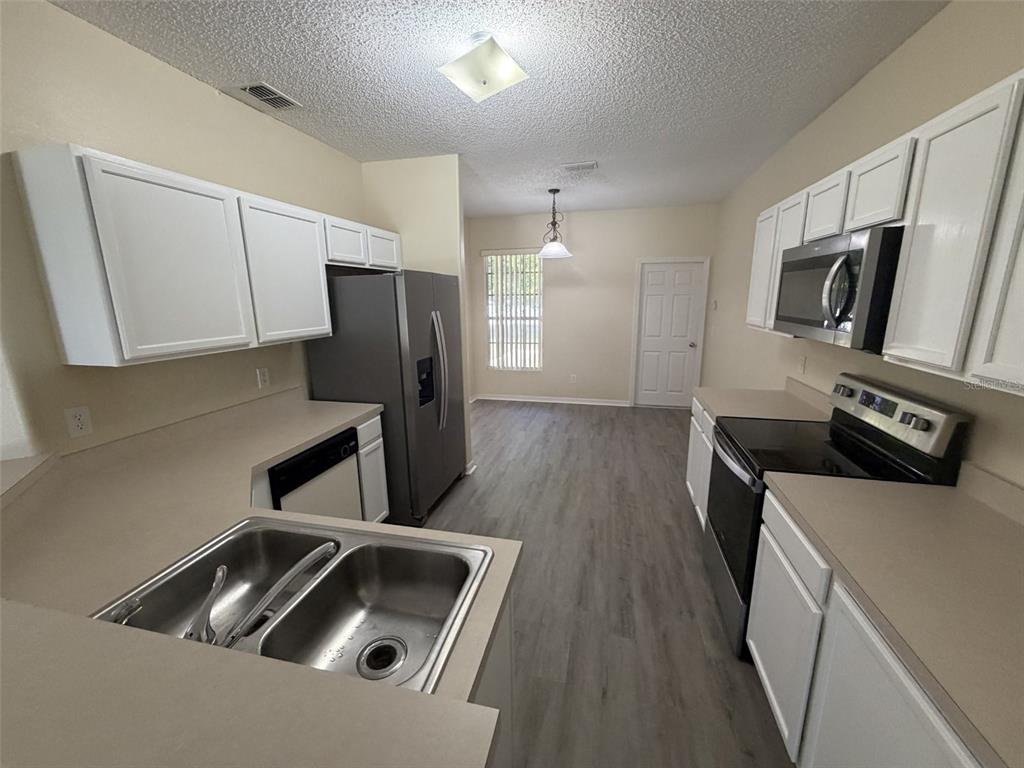 A kitchen features white cabinets, stainless steel appliances, a double sink, and wood-look flooring — 311 SUNSET VIEW DRIVE, DAVENPORT, FL