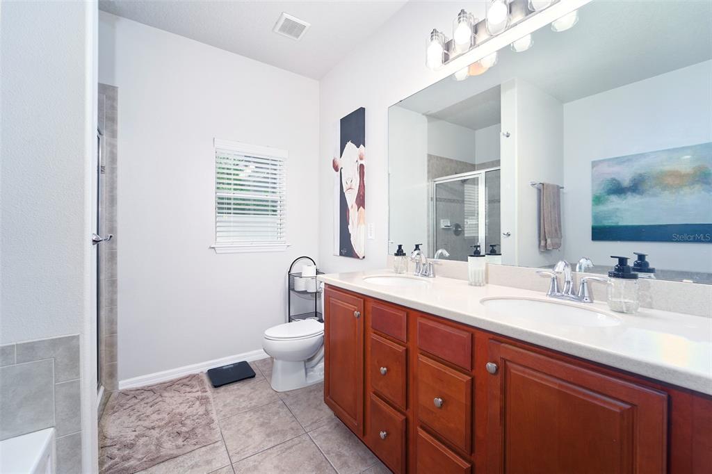 A bathroom features a double-sink vanity with wood cabinets, a toilet, and a shower stall — 2802 WINGLEWOOD CIRCLE, LUTZ, FL