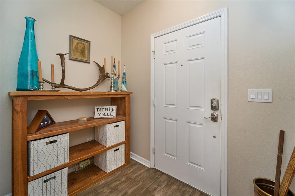 An entryway features a wooden bookshelf, a white door, and light wood-look flooring — 2802 WINGLEWOOD CIRCLE, LUTZ, FL