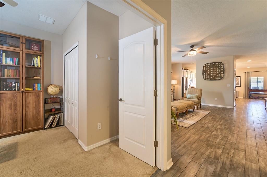 A carpeted room with a wooden bookcase connects to a tiled living area through a doorway — 2802 WINGLEWOOD CIRCLE, LUTZ, FL