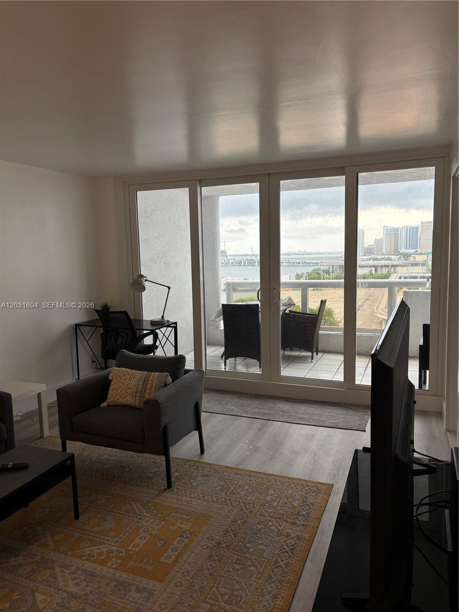 A living room with a desk, gray armchair, and sliding glass doors leading to a balcony — 1717 N Bayshore Dr # 1652, Miami FL 33132, MIAMI, FL