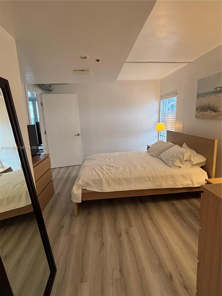 A bedroom features a wooden bed frame, light wood-look flooring, and a large floor mirror — 1717 N Bayshore Dr # 1652, Miami FL 33132, MIAMI, FL