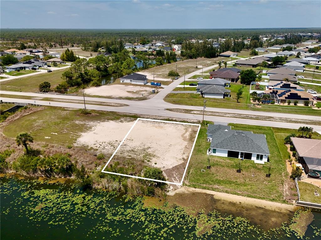 An aerial view shows a vacant, rectangular waterfront lot outlined in white next to a house — 900 VOGIANTZIS PARKWAY, CAPE CORAL, FL