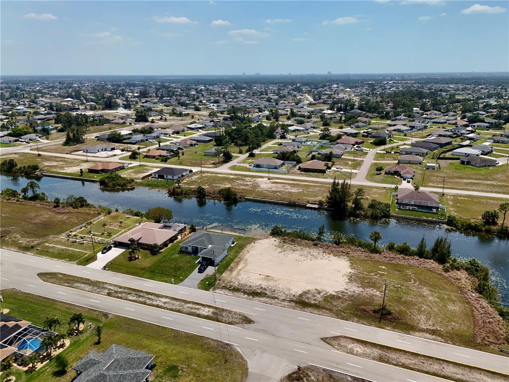 An aerial view shows a residential neighborhood with houses, a canal, and a vacant lot — 900 VOGIANTZIS PARKWAY, CAPE CORAL, FL