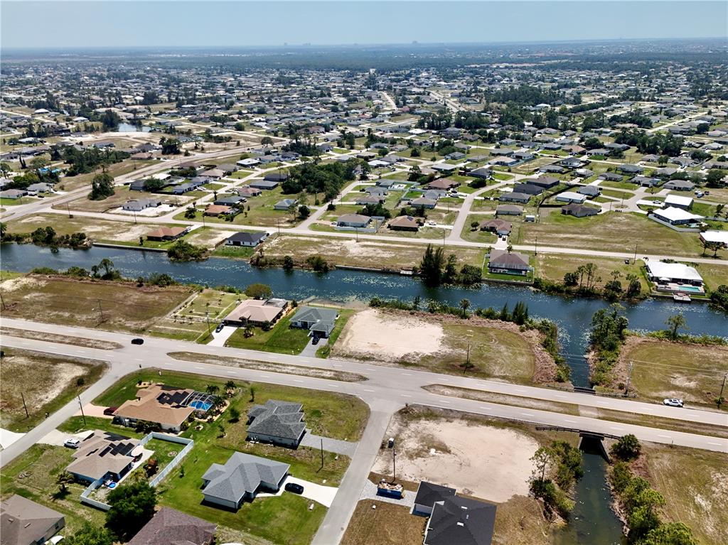 An aerial view shows a residential neighborhood with houses, a canal, and vacant lots — 900 VOGIANTZIS PARKWAY, CAPE CORAL, FL