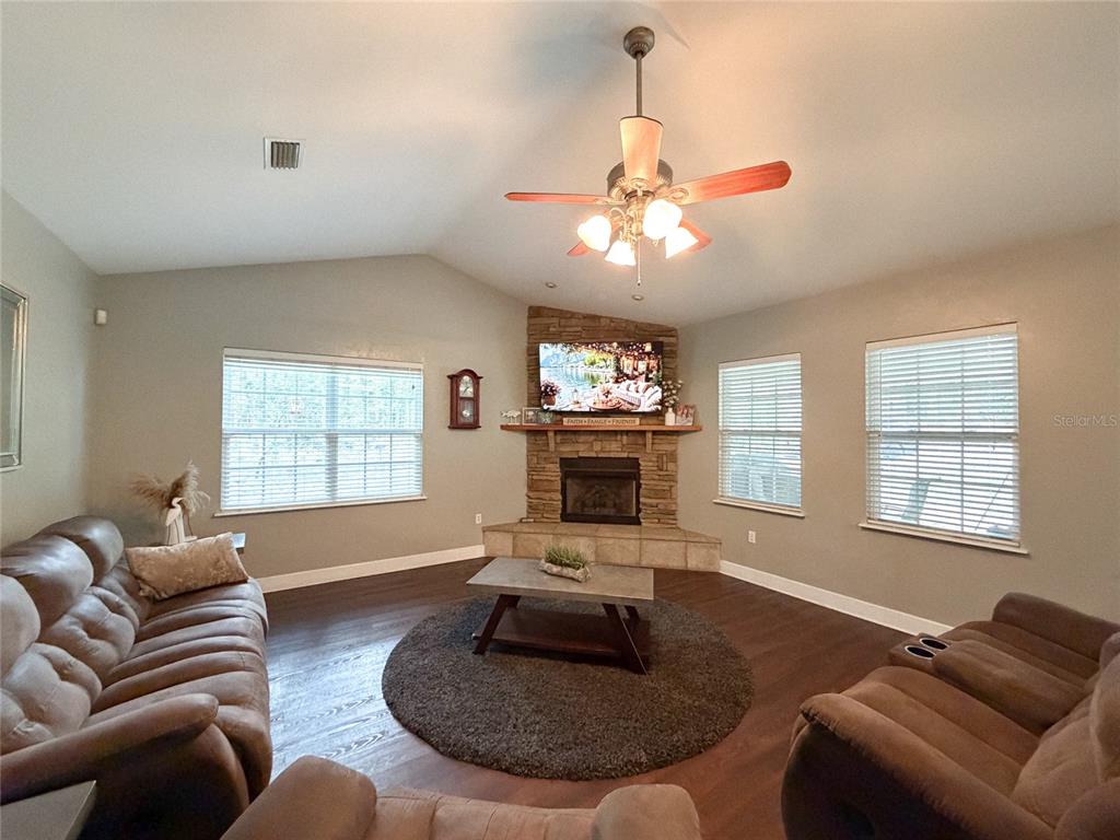 A living room features a corner stone fireplace, a ceiling fan, and brown furniture — 20942 NW 200TH AVENUE, HIGH SPRINGS, FL