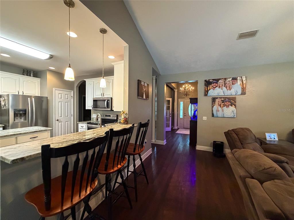 A kitchen with a breakfast bar and stools opens into a living room with hardwood floors — 20942 NW 200TH AVENUE, HIGH SPRINGS, FL