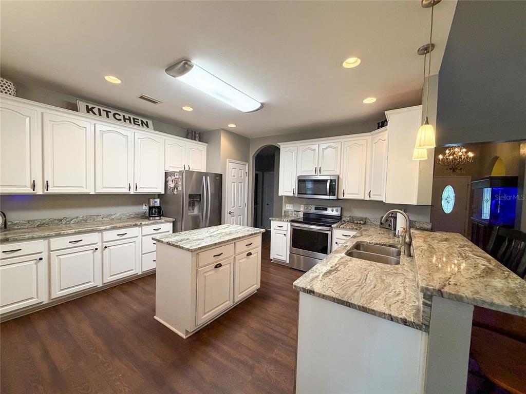 A kitchen features white cabinetry, granite countertops, a center island, and stainless steel appliances — 20942 NW 200TH AVENUE, HIGH SPRINGS, FL