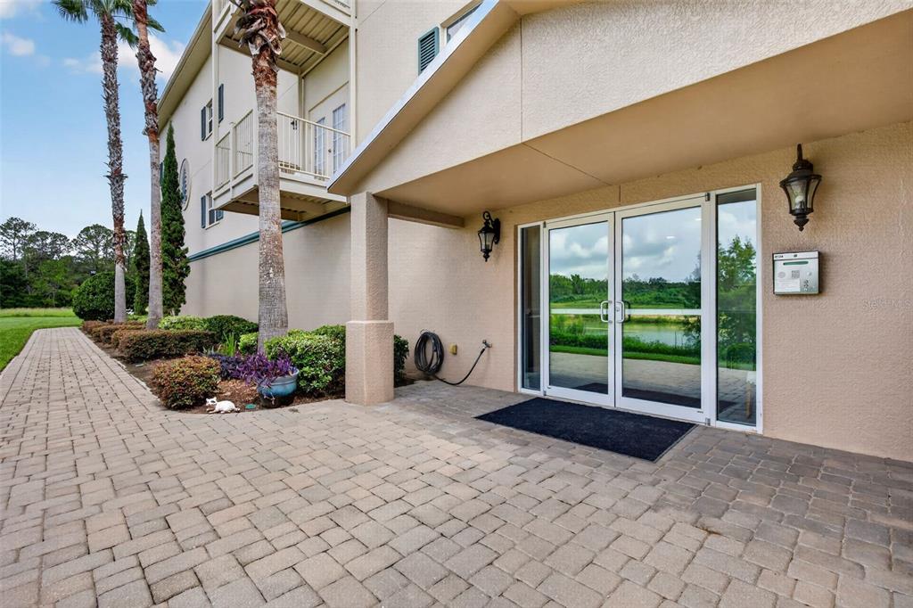 A paved walkway leads to the glass double-door entrance of a beige multi-story building — 7980 SOUTHERN PINES DRIVE, BROOKSVILLE, FL