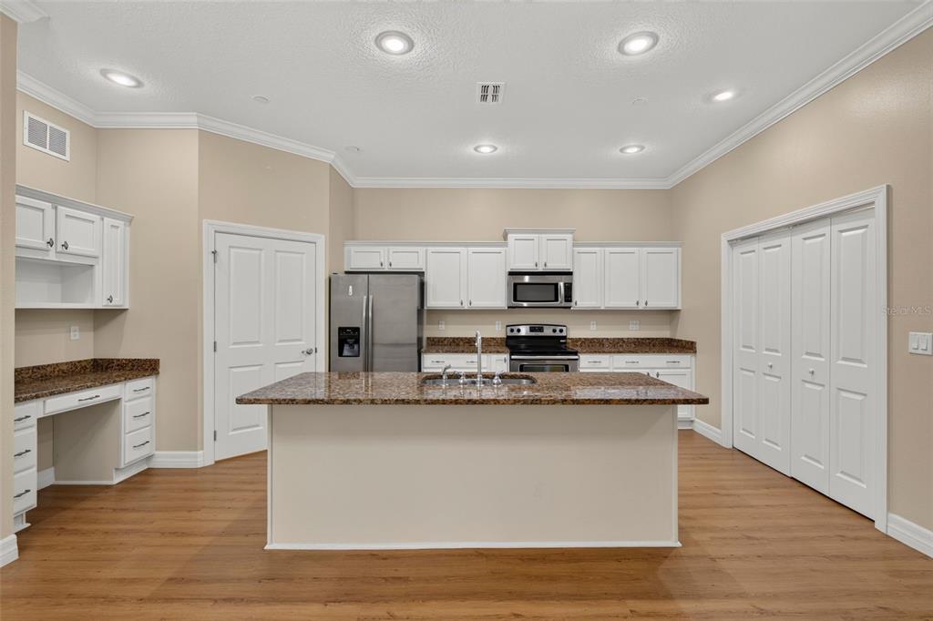 A kitchen features white cabinets, granite countertops, a central island, and wood-look flooring — 7980 SOUTHERN PINES DRIVE, BROOKSVILLE, FL