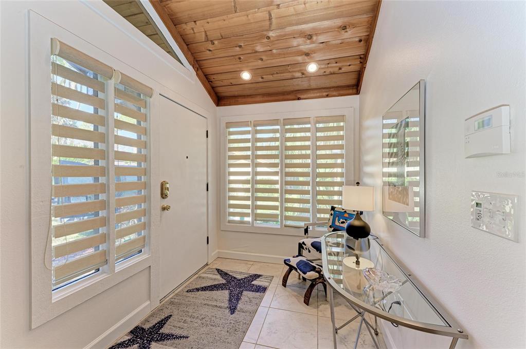 An entryway features a wood-paneled vaulted ceiling, tile flooring, a starfish rug, and glass furniture — 7921 4TH AVENUE W, BRADENTON, FL