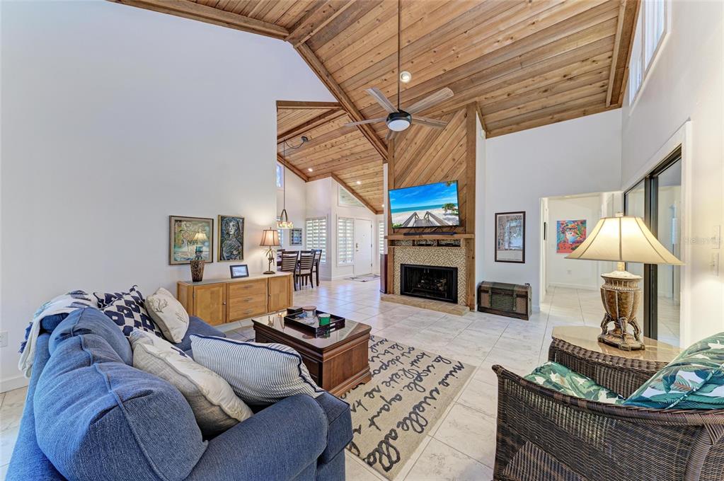 A living room features a vaulted wood-paneled ceiling, a fireplace with a television, and tile flooring — 7921 4TH AVENUE W, BRADENTON, FL