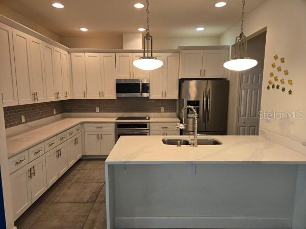 A modern kitchen features white cabinets, a large island, stainless steel appliances, and pendant lighting — 922 CENTAURY DRIVE, KISSIMMEE, FL