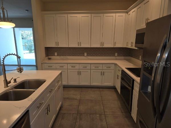 A kitchen features white cabinets, a quartz-topped island with a sink, and gray tile flooring — 922 CENTAURY DRIVE, KISSIMMEE, FL