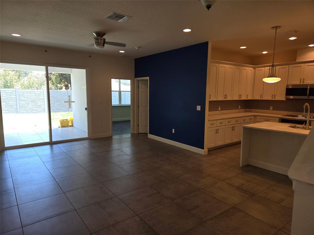 An open-concept kitchen with white cabinetry and an island overlooks a tiled living area — 922 CENTAURY DRIVE, KISSIMMEE, FL