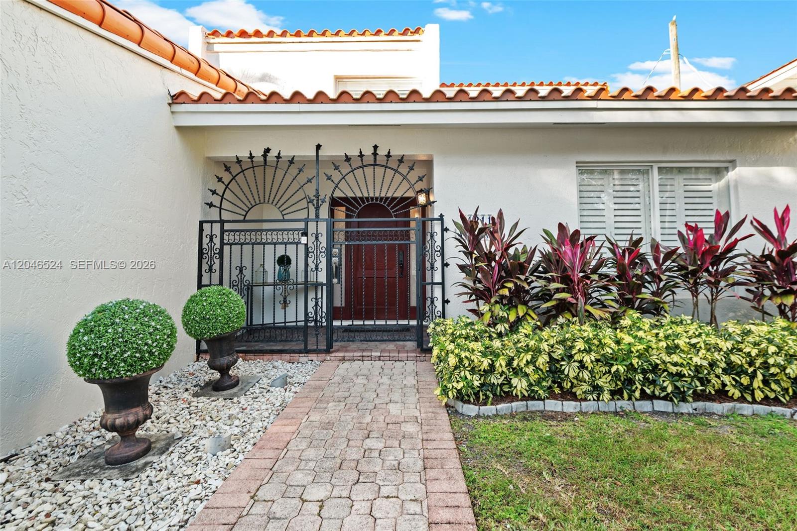 The exterior of a house features a brick walkway, wrought iron gate, and landscaping — 1211 Algeria Ave, Coral Gables FL 33134, CORAL GABLES, FL