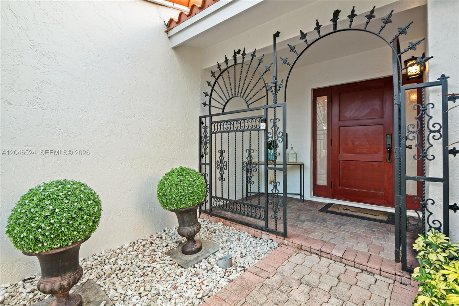 An exterior entryway features a decorative wrought iron gate, brick pavers, and two potted topiaries — 1211 Algeria Ave, Coral Gables FL 33134, CORAL GABLES, FL
