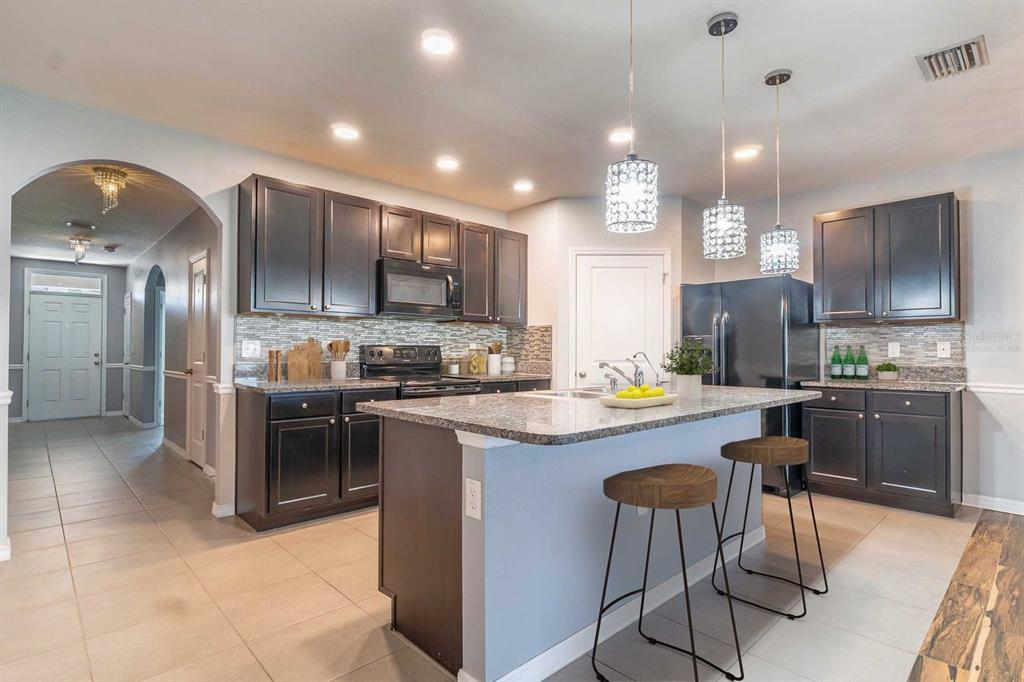 A kitchen with dark cabinets, granite countertops, a central island, and two bar stools — 10662 PARK MEADOWBROOKE DRIVE, RIVERVIEW, FL