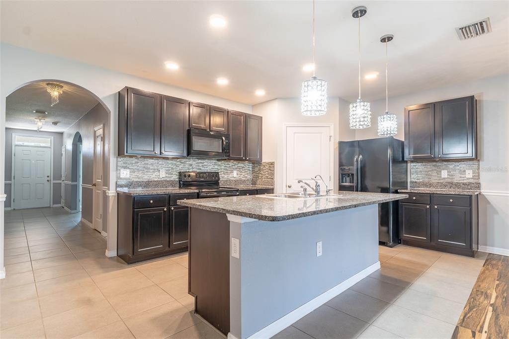 A kitchen features dark wood cabinets, granite countertops, a central island, and stainless steel appliances — 10662 PARK MEADOWBROOKE DRIVE, RIVERVIEW, FL