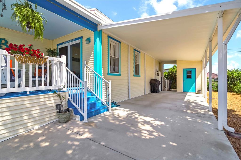 A yellow house exterior features a covered carport, blue stairs, and a white porch railing — 915 50TH AVENUE W, BRADENTON, FL
