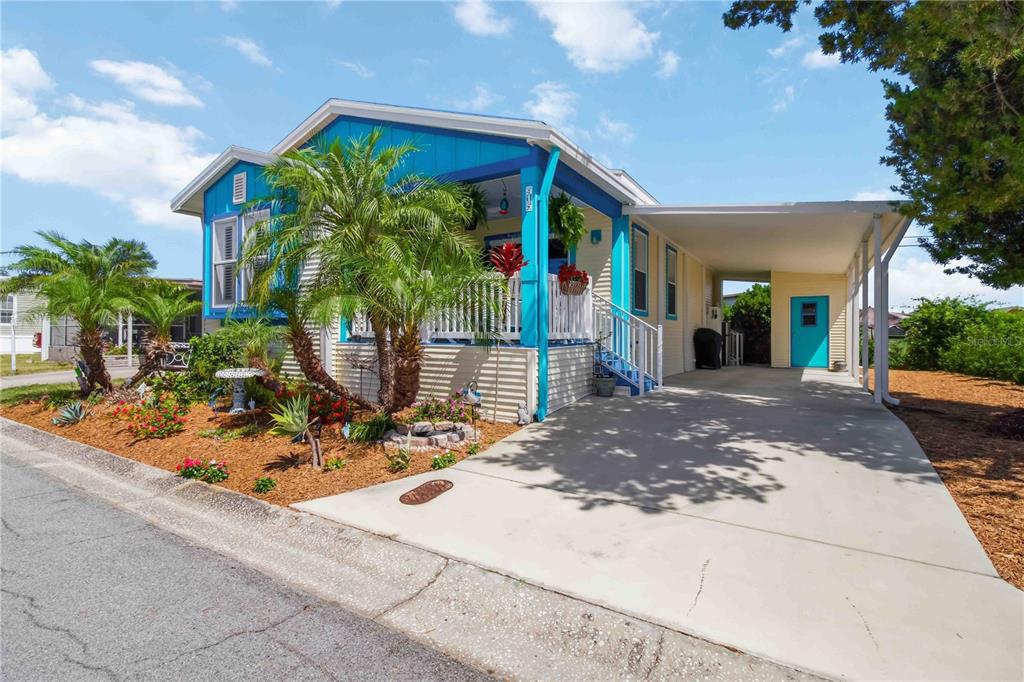 A blue and beige manufactured home features a front porch, palm trees, and a carport — 915 50TH AVENUE W, BRADENTON, FL